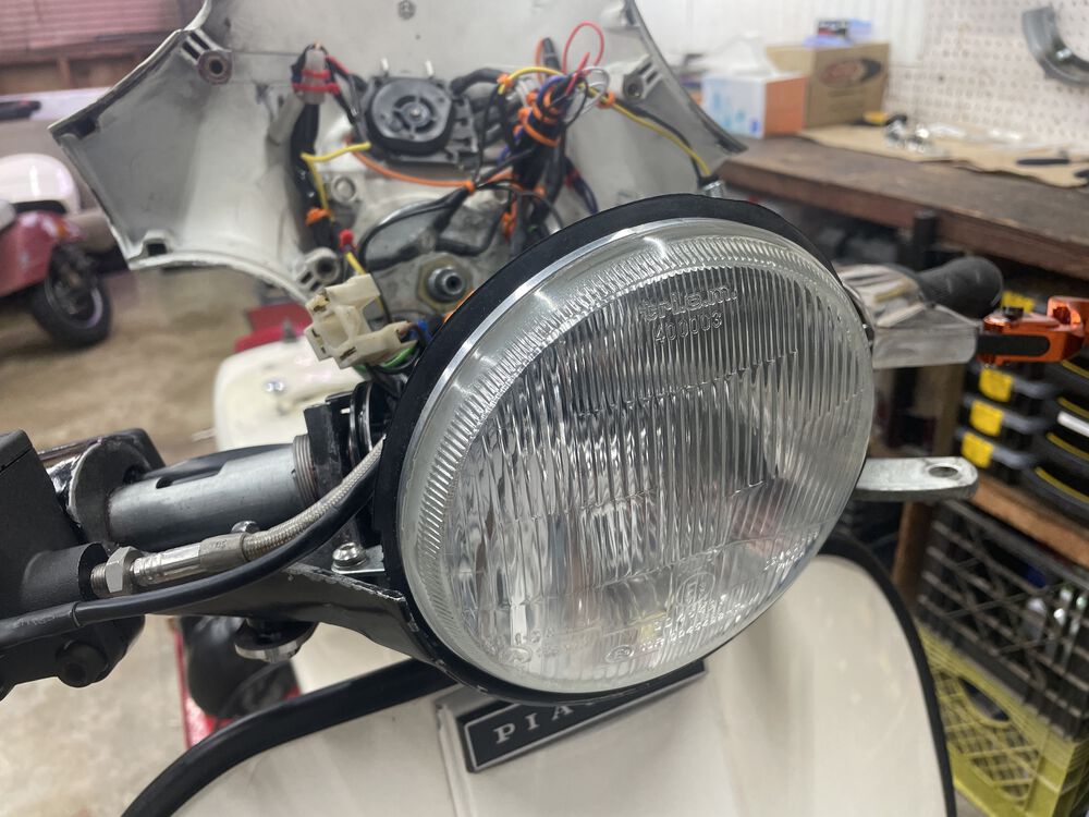 New COSA headlight unit. The housing has a glass lens, plastic back; and is a direct fit. Takes an H4 bulb. I'm using a standard halogen for now.
