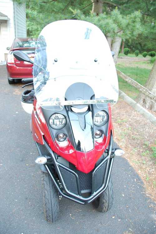 FIG 3:The cruiser sheild on the MP3. Note the vertical straps are gone, and the horizontal strap has been moved down to cross what used to be the windshield's headlight cutout. The two black circles higher up are the grommets from the GIVI, in new holes.